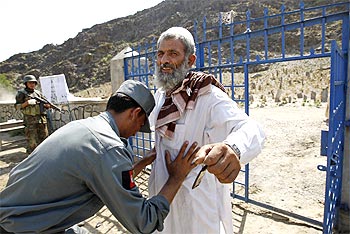 An Afghan policeman searches a local villager in front of the polling station in the village of Mangwal in Kunar province