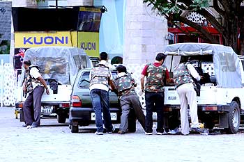 Police personnel take cover behind vehicles during the stand-off at Taj hotel