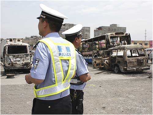 Policemen stand in front of vehicles, which were destroyed during Sunday riot in Urumqi