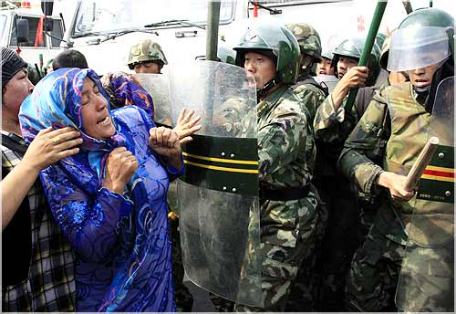 A woman pushes at Chinese soldiers wearing riot gear as a crowd of angry locals confront security forces on a street