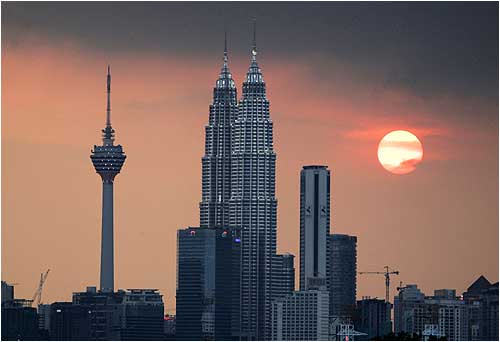 The sun sets near the Petronas Twin Towers (C) and Kuala Lumpur Tower