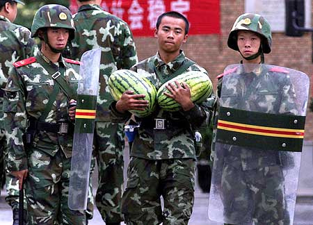 A Chinese soldier carries two watermelons as he walks past two fellow soldiers in riot gear guarding a mosque in the city of Urumqi