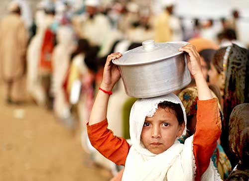 An internally displaced girl, fleeing military operations in the Swat valley region, holds a pot over her head while standing in line for curry and bread at the UNHCR camp