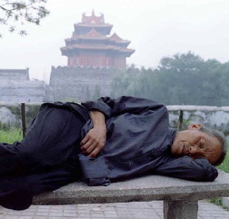 An elderly Chinese woman naps on a park bench near the Forbidden City in China