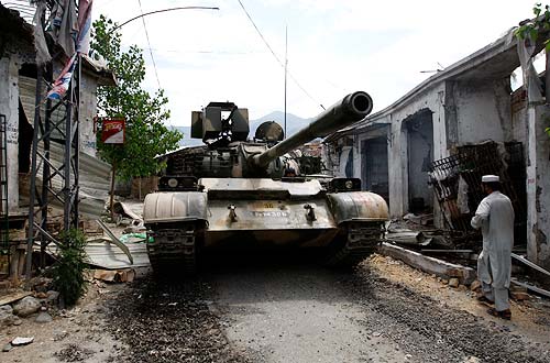 A tank passes through a street past damaged shops at Maidan at Lower Dir district in the Swat region on June 13