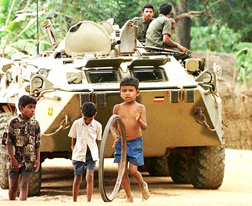 Tamil children in a refugee camp play with a bicycle rim in front of a Sri Lankan battle tank