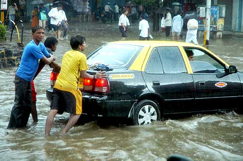 People push a cab stranded in rain-water