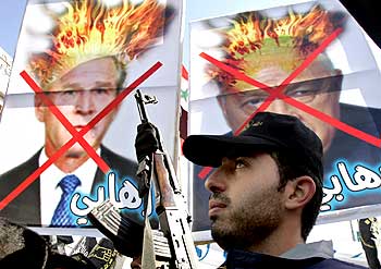 A Palestinian holds his rifle near photographs of then US President George W Bush and then Israeli Prime Minister Ariel Sharon, with 'terrorist' written on them, during a demonstration in the Gaza Strip on November 18, 2005.