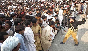 A policeman threatens to strike a man, who was fleeing a military offensive in South Waziristan, for jumping a queue at a food distribution point