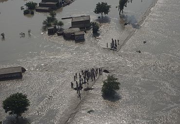 Residents stand near the path of flowing flood waters the Muzaffargarh district of Pakistan's Punjab province
