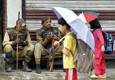 Kashmiri children carrying umbrellas walk past policemen during a shutdown