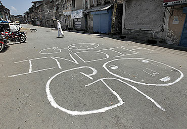 A Kashmiri man crosses a deserted road marked with graffiti