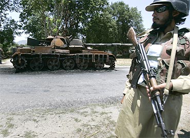 A Pakistani soldier stands guard next to an army tank destroyed by militants in Buner district