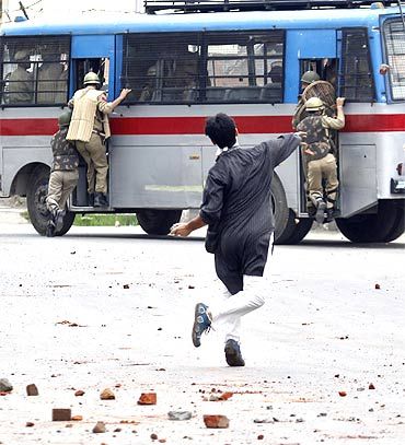 A Kashmiri protestor pelts stones on a bus carrying police personnel
