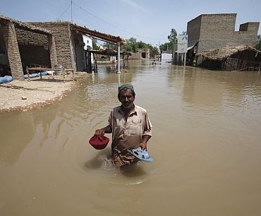 Ali Hassan, a villager, holds his sandals and meal as he wades through floodwaters in Amri village, some 280 km from Karachi