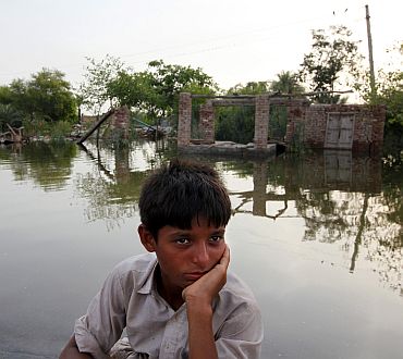 A boy sits in front of a house destroyed by floodwaters in a village in Muzaffargarh district