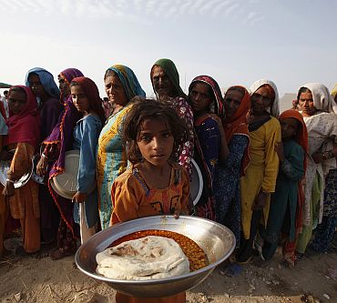 Anila, a flood victim, holds up a plate of food as others queue in a makeshift relief camp in Sukkur, in Sindh province
