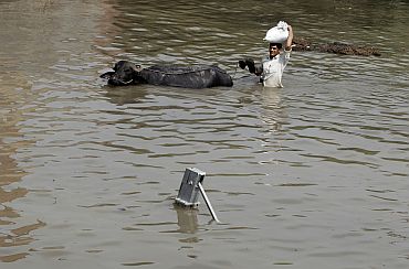 A local resident carries belongings with his buffalo through a flooded road in New Delhi on Tuesday