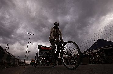 A cycle rickshaw puller is silhouetted against the backdrop of monsoon clouds in New Delhi on Tuesday