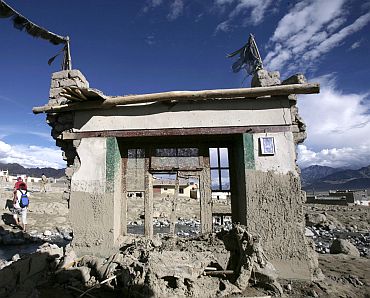 People walk near damaged houses after flash floods occurred on the outskirts of Leh