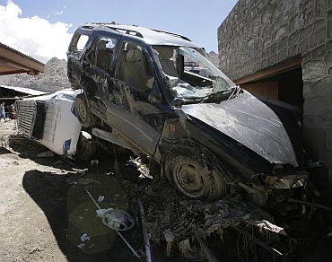 Flash flood victims walk near the wreckage of damaged cars after flash floods in Leh