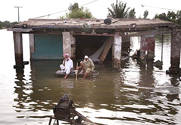 Flood victims sit in front of their destroyed shop in Pakistan's Muzaffargarh district