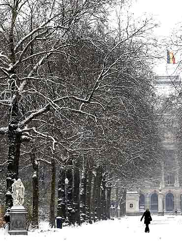 A woman walks towards the snow-covered Royal Park in front of The Royal Palace in Brussels