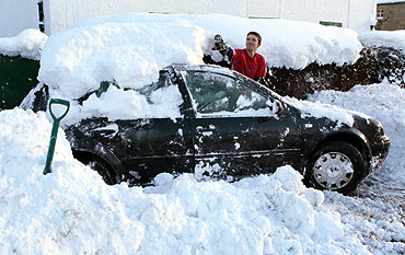 David Morran clears snow off his car as he trys to free it out of the driveway of his home in Braco, Scotland