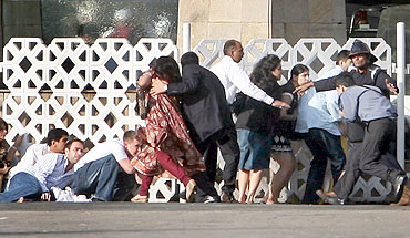 People duck as gunshots are fired from inside the Taj Mahal hotel in Mumbai during the 26/11 terror attacks
