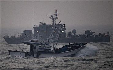 A fishing boat sails past a South Korean navy ship patrolling off Yeonpyeong Island
