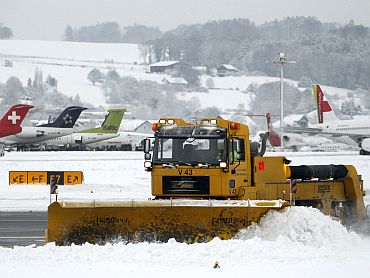 Workers use a snowplough to remove snow from the tarmac of Zurich airport