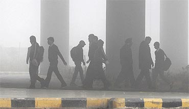 Airport staff walk towards the main terminal amid heavy fog in New Delhi