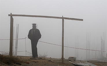 A security staff stands guard at a construction site amid heavy fog near the airport in New Delhi