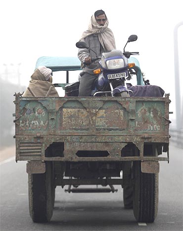 A man sits on his motorcycle on a trailer attached to a tractor on a foggy morning in New Delhi