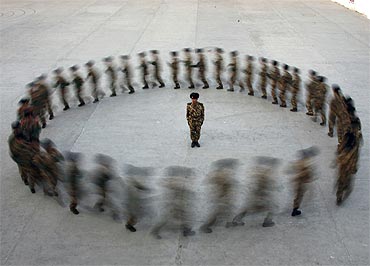 A commander watches as recruits of paramilitary police run in a circle during a training at a military base in Hami, Xinjiang