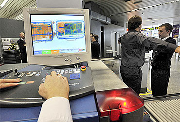 Security personnel check a passenger and his bags through an X-ray machine