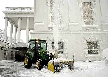 A snow blower clears snow from a driveway around the White House