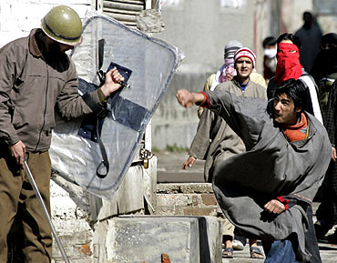 A Kashmiri protester throws a rock towards a state police officer during a protest in Srinagar