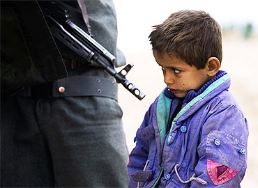 An Afghan boy looks on as his father is searched by a policeman at a checkpoint at Delaram district in Nimroz province, southern Afghanistan