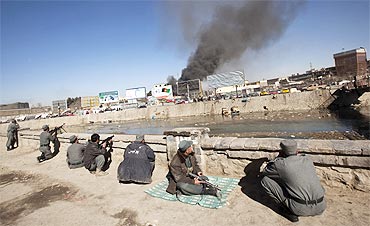 Afghan policemen take positions as smoke rises from a shopping mall