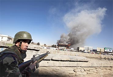 An Afghan National Army soldier takes position as smoke rises from a shopping mall