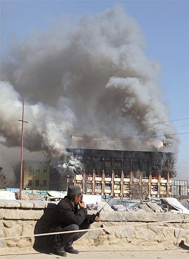 Smoke rises from a shopping mall as a policeman speaks on his radio during the Taliban attack