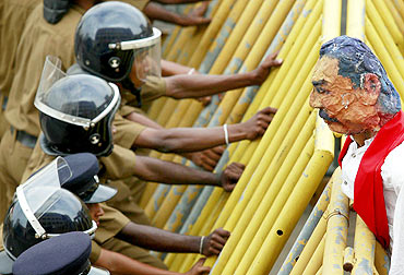 Police take up position behind a metal barrier as students from a group of universities hold a puppet of Rajapaksa over the barrier during a protest in Colombo