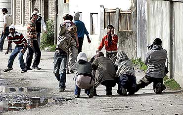 A Kashmiri protester throws stones towards policemen as foreign photographers take pictures