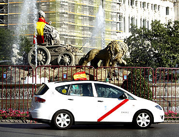A taxi with a Spanish flag drives past the Cibeles statue wrapped in another flag in Madrid, July 9