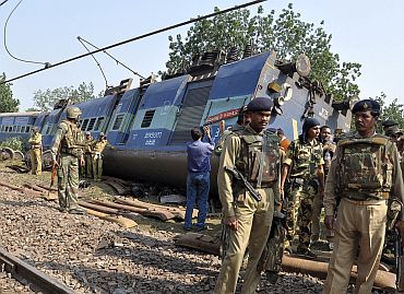 Police and railway officials stand next to an overturned coach of the passenger train