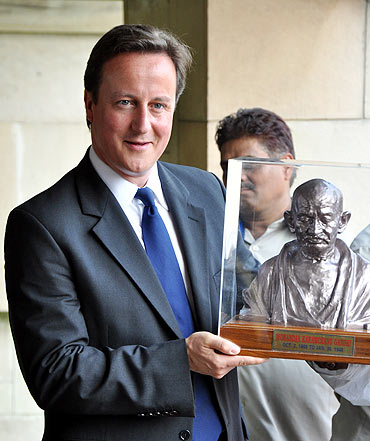 Cameron holds a bust of Mahatma Gandhi at Rajghat in New Delhi on Thursday