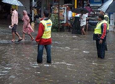 Municipal workers assist people wading through a water-logged street