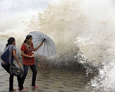 Women use an umbrella to protect themselves during high tide at Mumbai's seafront