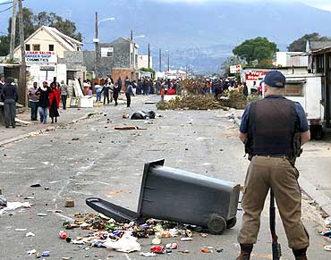 A police officer stands guard as protesting residents unhappy with living conditions look on at Masiphumelele informal settlement in Cape Town, on July 30, 2009